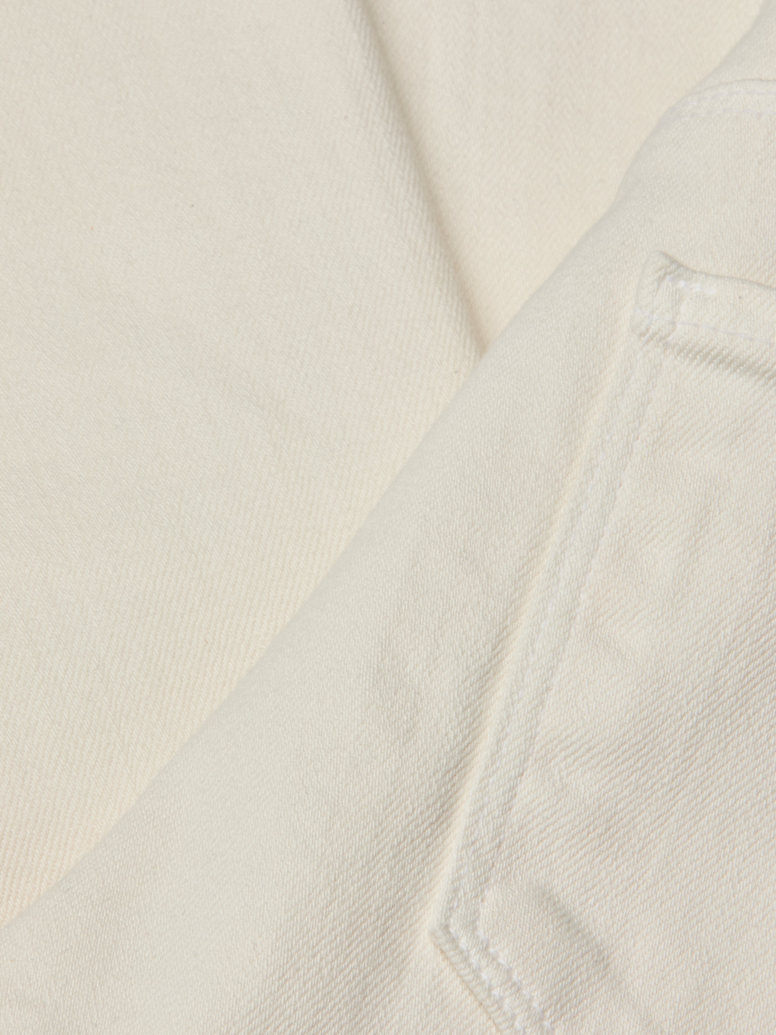 Close-up of off-white or cream-colored denim fabric, highlighting a pocket and visible stitching details on the Alicent Wide-Leg Jean. The texture and weave of the high-rise, wide-leg jean’s fabric are clearly shown.