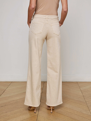 A person wearing L'AGENCE Alicent Wide-Leg Jeans in a high rise, sneaker-length fit with nude heels stands on a light wood floor, facing away from the camera against a plain white wall.