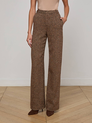 Indoors, a person wears L'AGENCE Livvy Straight-Leg Trousers in brown Italian recycled wool, hands in pockets. They're styled with brown pointed-toe heels and a sleeveless beige top against a plain setting with light wood floors.
