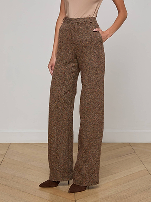 A person stands on a wooden floor wearing L'AGENCE Livvy Straight-Leg Trousers in a brown pattern, paired with a sleeveless beige top and brown pointed-toe heels. One hand is in their pocket; their face is not visible.