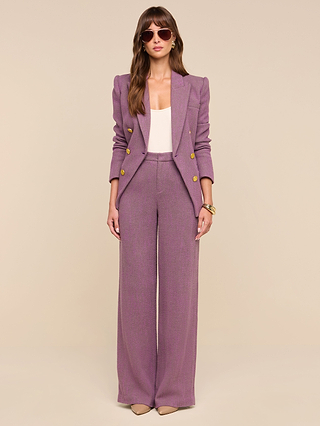 Wearing the Livvy Straight-Leg Trouser with a matching mauve blazer adorned with gold buttons, a woman pairs her high-rise ensemble with a white top, nude heels, sunglasses, and gold bracelets as she stands against a beige background.