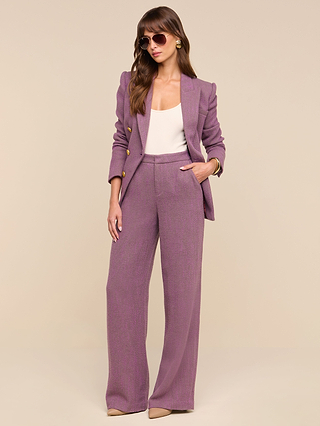 A woman stands confidently with one hand in her pocket against a plain beige background, wearing the Livvy Straight-Leg Trouser in mauve herringbone, paired with a white top, beige heels, and sunglasses.