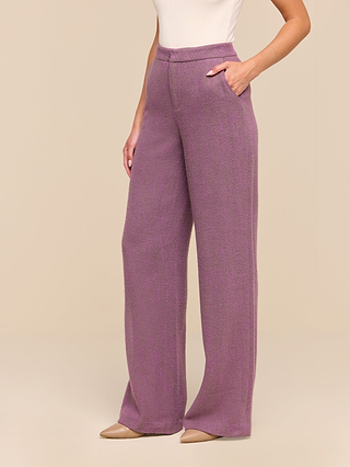 A person wearing the Livvy Straight-Leg Trouser in a high-waisted, wide-leg purple herringbone style with hands in the pockets, paired with beige pointed-toe shoes and a sleeveless white top, standing against a plain beige background.