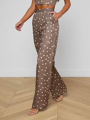 A woman is seen indoors from the waist down wearing Livvy Straight-Leg Trousers, featuring a brown polka dot pattern, paired with a matching crop top.