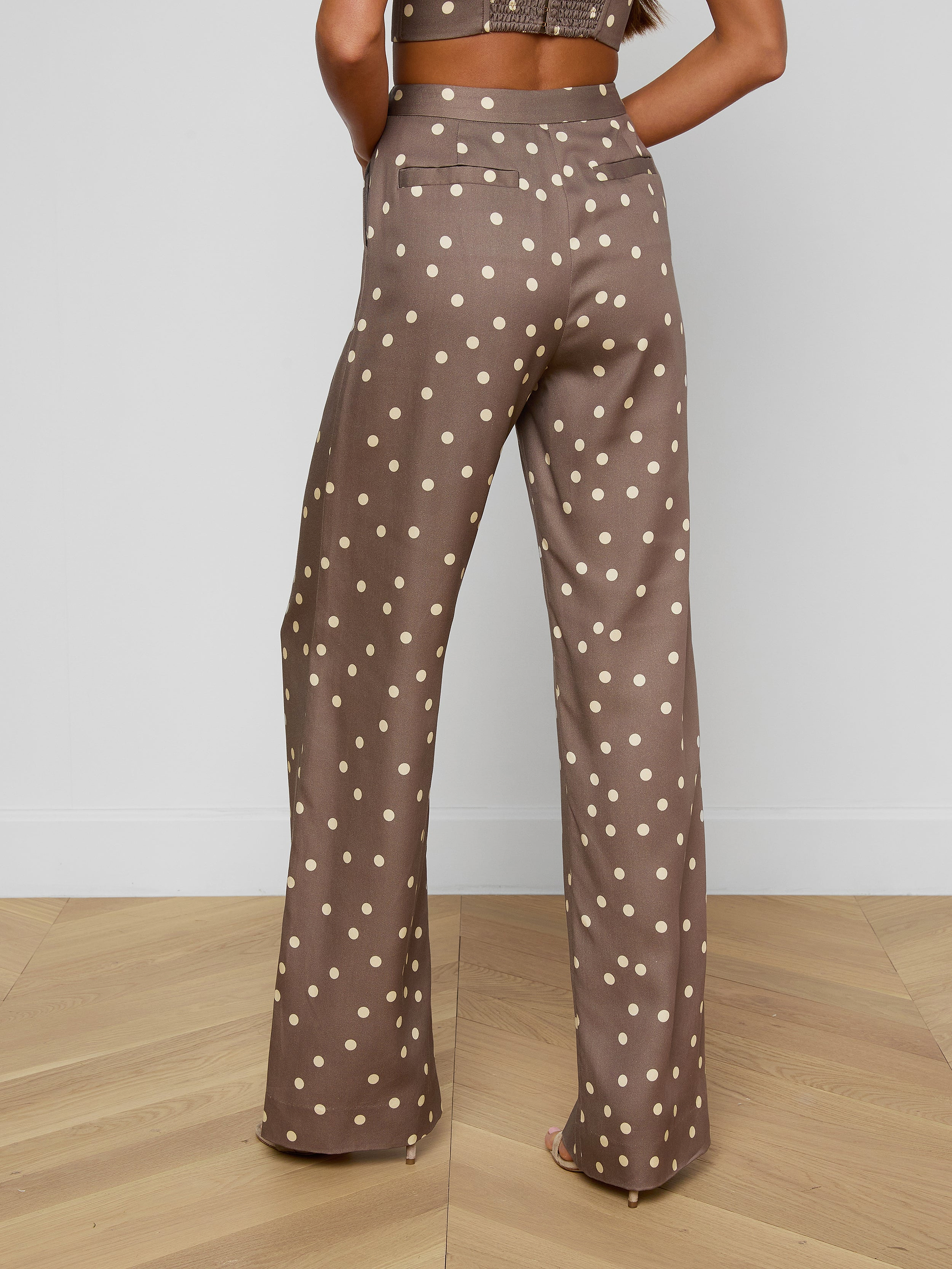 Wearing the Livvy Straight-Leg Trouser, a person stands facing away. The high-rise brown trousers feature a polka dot print and are styled with heeled sandals and a coordinating cropped top.