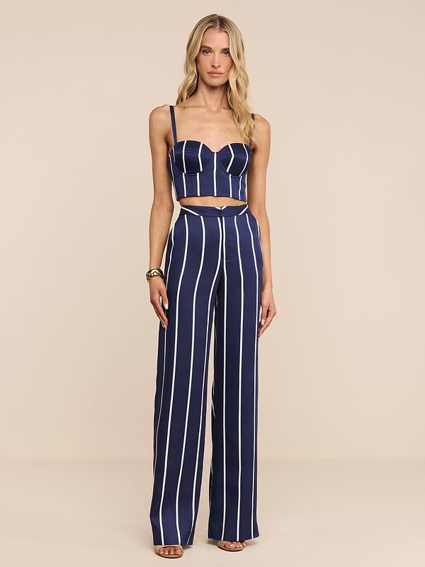 Una donna si staglia su uno sfondo semplice indossando i pantaloni Livvy, caratterizzati da audaci strisce verticali bianche e da una silhouette a gamba larga. Abbina questi pantaloni in tencel navy a sandali con tacco alto e porta i lunghi capelli biondi ondulati sciolti.