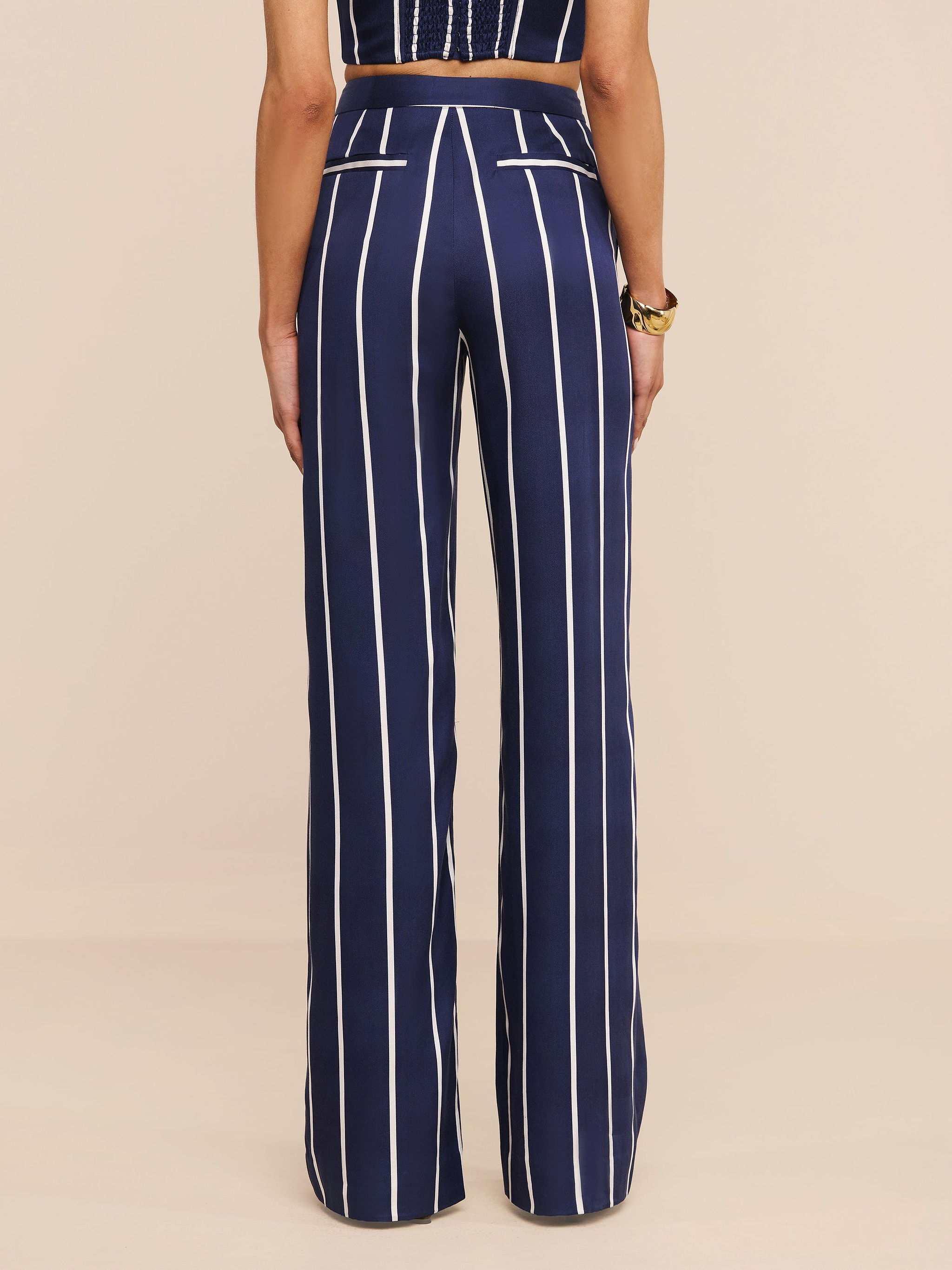 Una persona indossa i pantaloni Livvy - pantaloni a vita alta e a gamba larga in tencel leggero, con strisce verticali bianche e tasche posteriori bordate di bianco. Mostrati da dietro, abbinati a un top senza maniche.