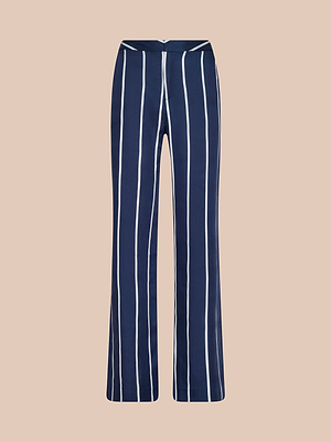 Le pantalon Livvy est en Tencel léger marine avec des rayures verticales blanches, une taille haute, une coupe droite et une fermeture à glissière sur le devant, sur un fond beige clair.