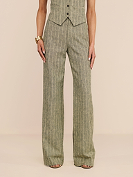 A person stands against a white background, wearing the high-waisted Livvy Linen-Blend Trouser in sage green pinstripes paired with a matching vest. Their look is completed with strappy heels and a chunky gold bracelet.