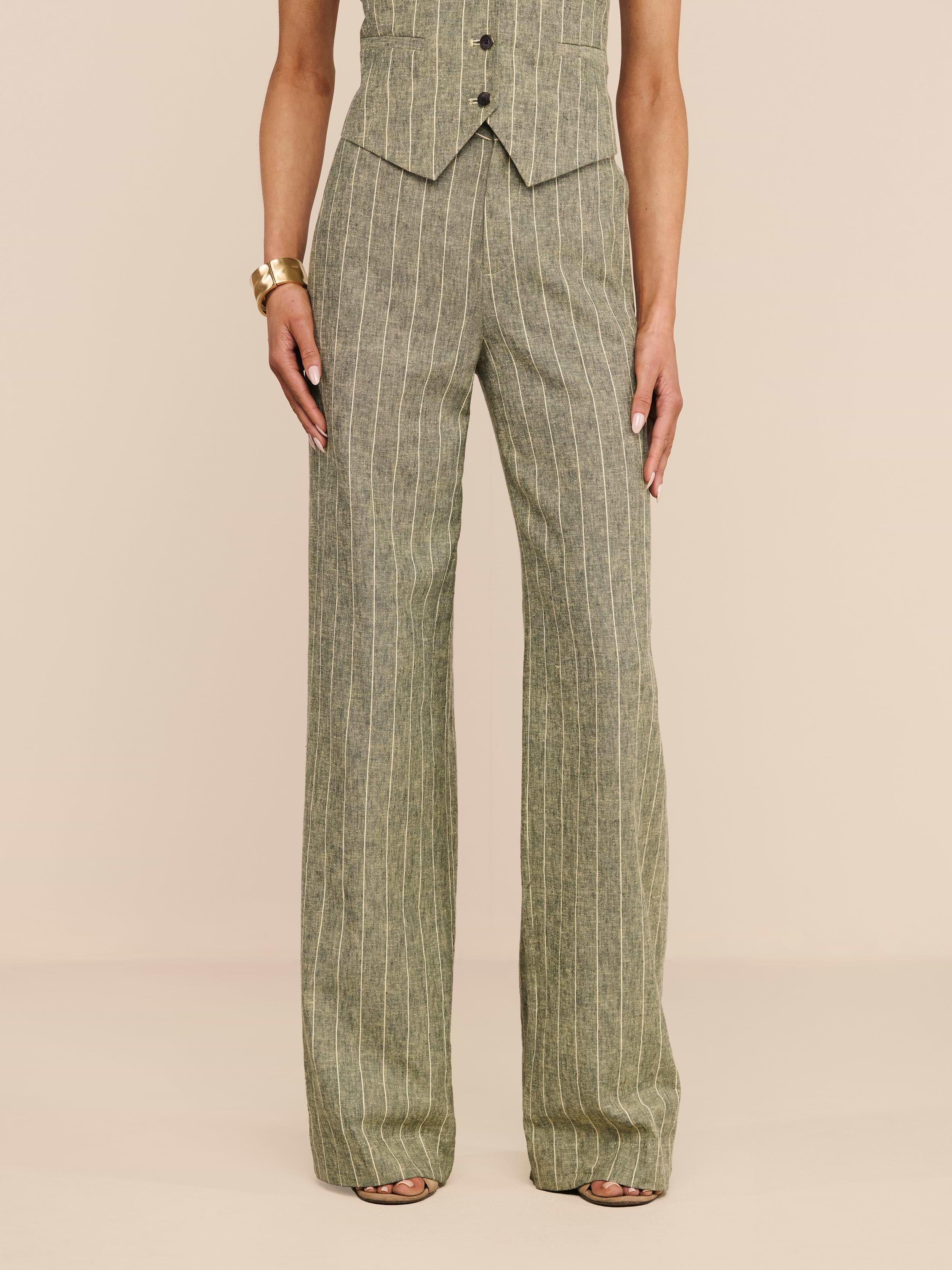 A person stands against a white background, wearing the high-waisted Livvy Linen-Blend Trouser in sage green pinstripes paired with a matching vest. Their look is completed with strappy heels and a chunky gold bracelet.