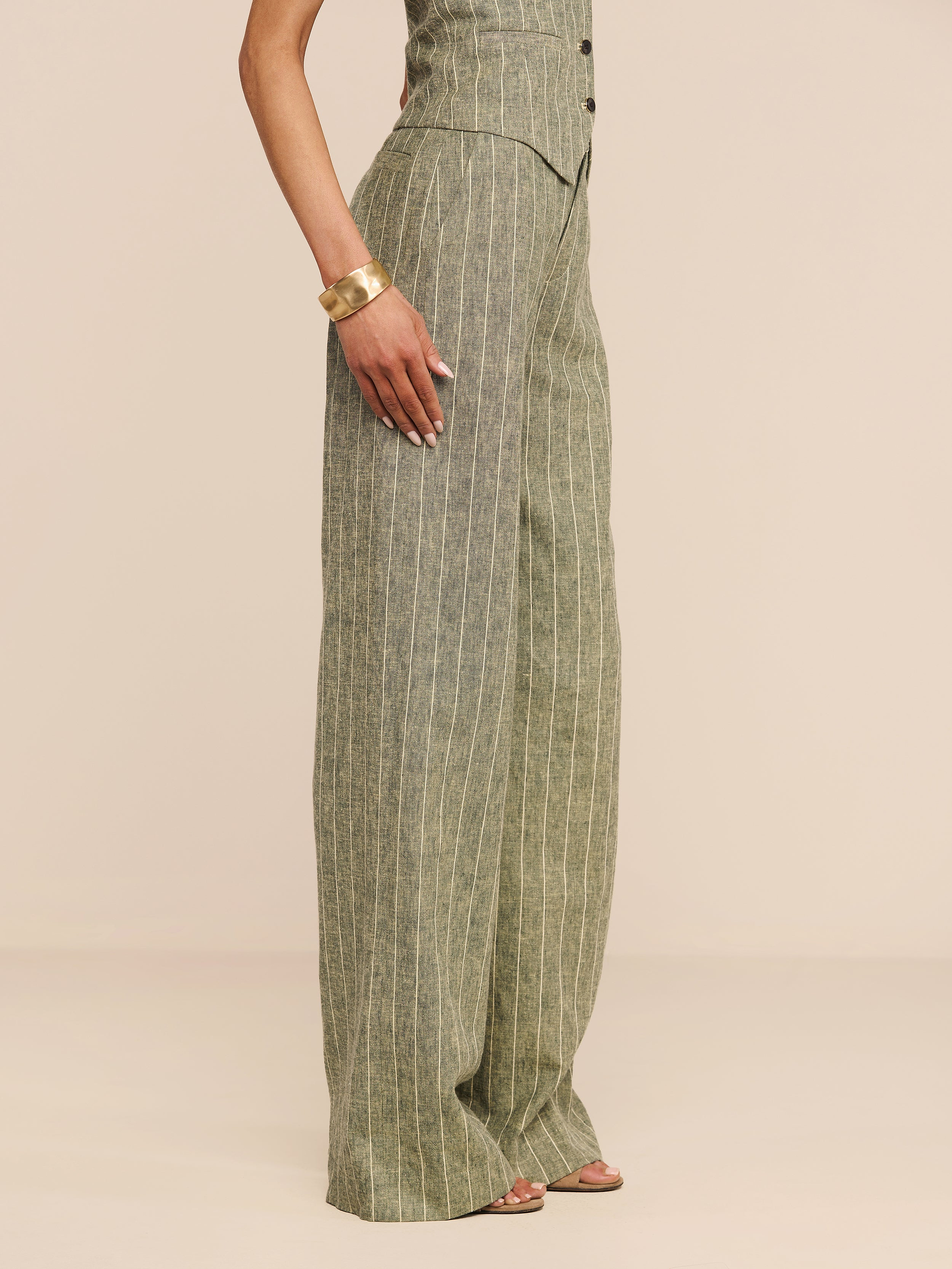 Wearing the Livvy Linen-Blend Trouser, styled with a matching top, gold bracelet, and sandals, a person stands against a plain white background.