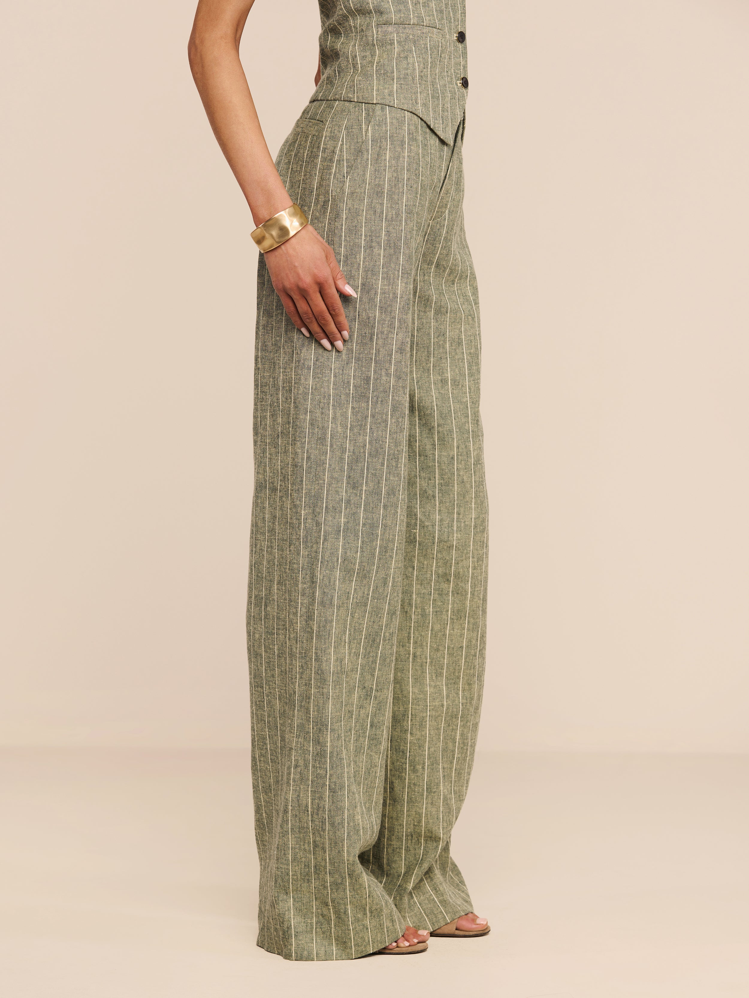 Wearing the Livvy Linen-Blend Trouser, styled with a matching top, gold bracelet, and sandals, a person stands against a plain white background.