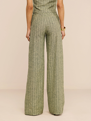Une personne regarde au loin, portant le pantalon Livvy Linen-Blend - taille haute, vert olive, jambe large avec des rayures verticales blanches - et un haut sans manches assorti ; la tenue est agrémentée dun bracelet en or.