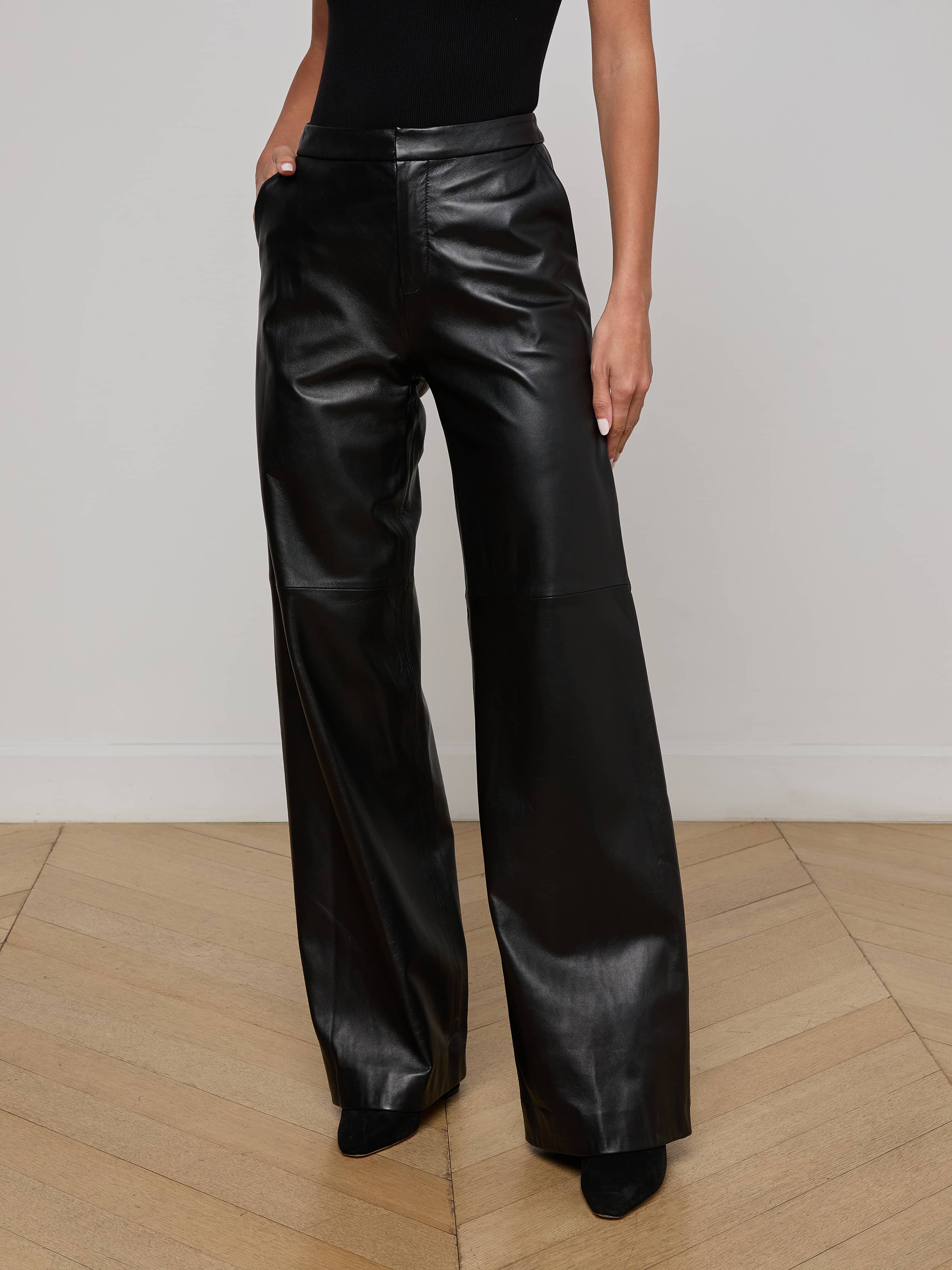A person wearing the Livvy Leather Trouser—a pair of high-waisted, wide-leg black lambskin leather pants—with hands in pockets, paired with a black top, against a plain light background.
