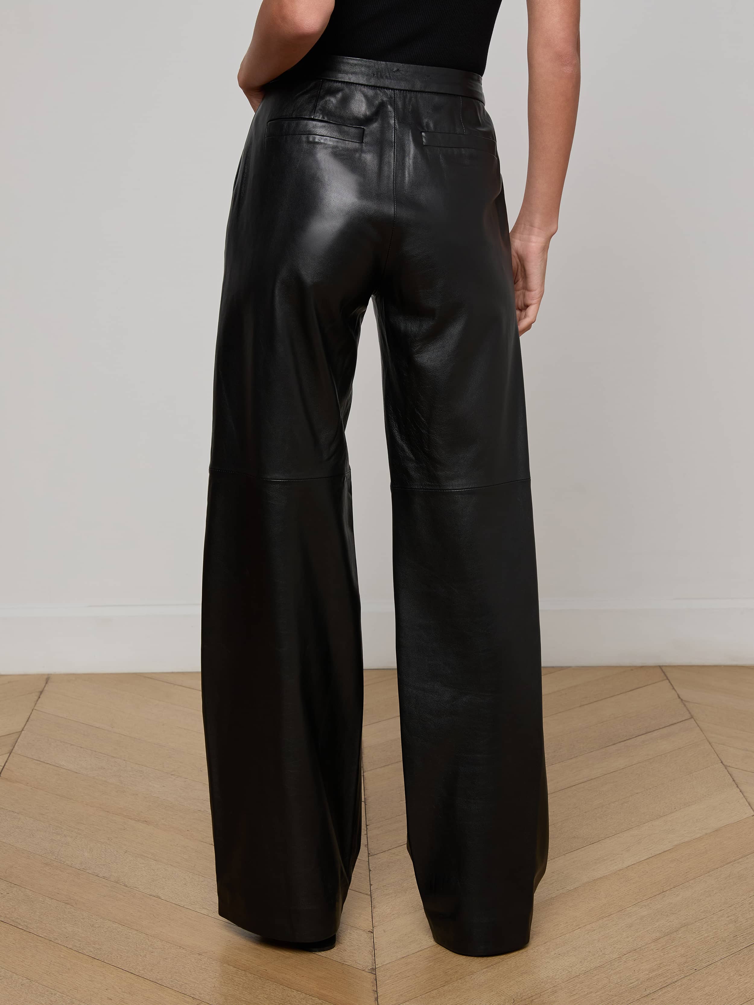 A person wearing the Livvy Leather Trouser—a high-waisted, wide-leg lambskin leather pant—shown from the back with one arm resting at their side against a plain light background.