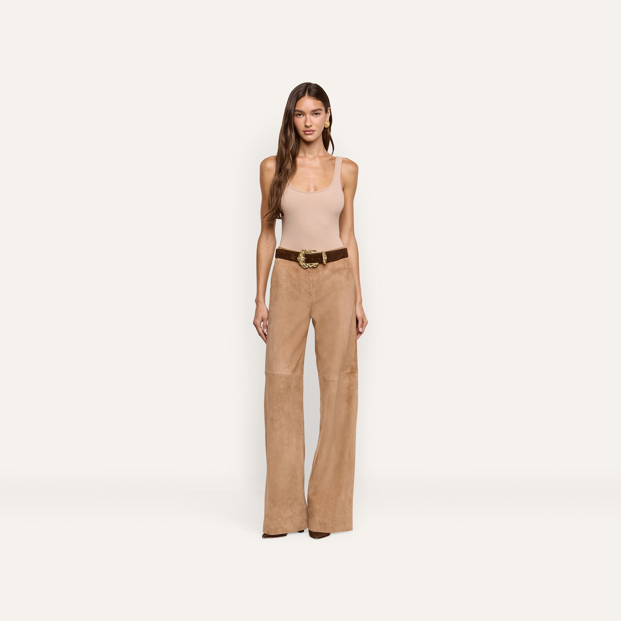 A woman wears a beige tank top and Livvy Suede Straight-Leg Trouser in a business casual style, paired with a brown belt featuring a gold buckle.