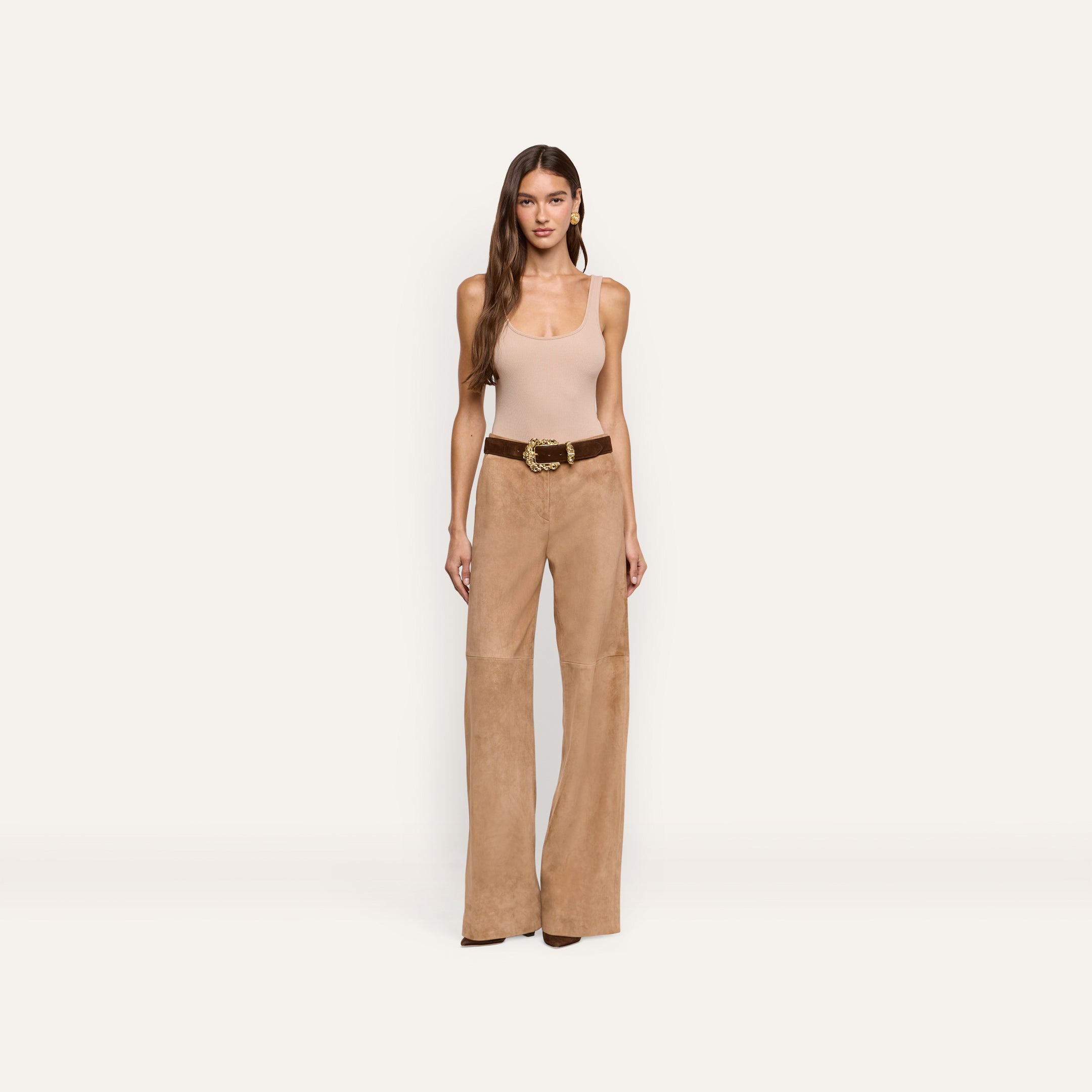 A woman wears a beige tank top and Livvy Suede Straight-Leg Trouser in a business casual style, paired with a brown belt featuring a gold buckle.