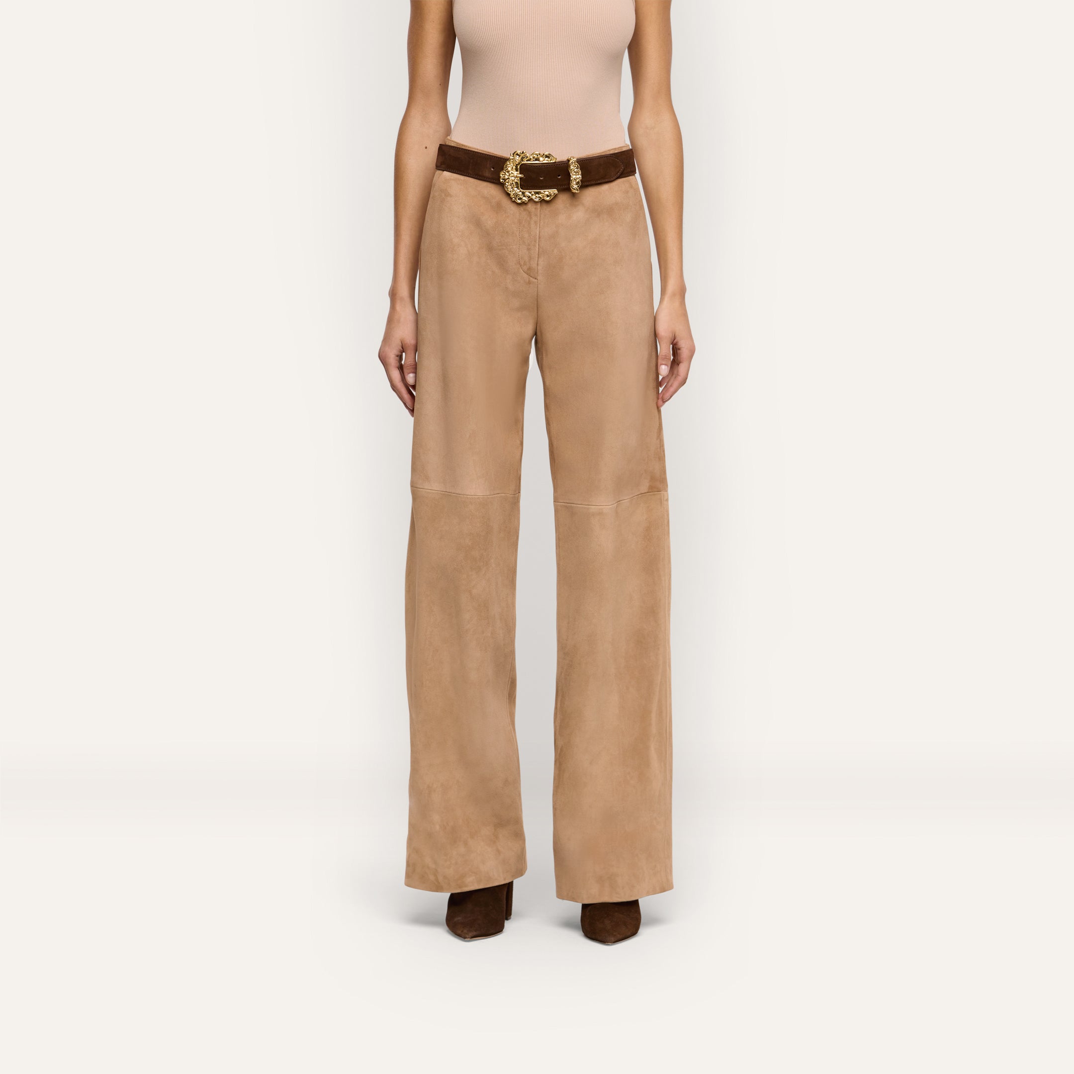 A person wearing beige suede Livvy Suede Straight-Leg Trousers for business casual wear, styled with a brown belt featuring a large gold buckle and brown shoes.