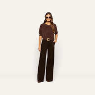 Woman wearing sunglasses, a loose brown sweater, and the Livvy Suede Trouser—a pair of high rise black wide-leg pants with a belt—standing against a plain light background with one hand in her pocket.