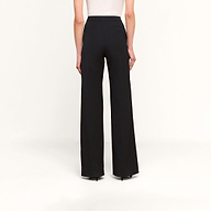 Une personne vue de dos sur un fond beige uni, portant le pantalon Livvy — un pantalon noir à taille haute et à jambes larges — associé à un haut blanc sans manches.