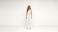 A woman wearing sunglasses, a sleeveless white top, and white wide-leg pants stands against a plain white background.