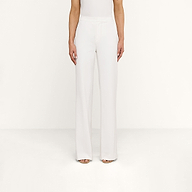 A person wearing the Livvy Trouser, a pair of high-rise, wide-leg white trousers, and open-toe heels stands against a plain white background with their arms relaxed by their sides.