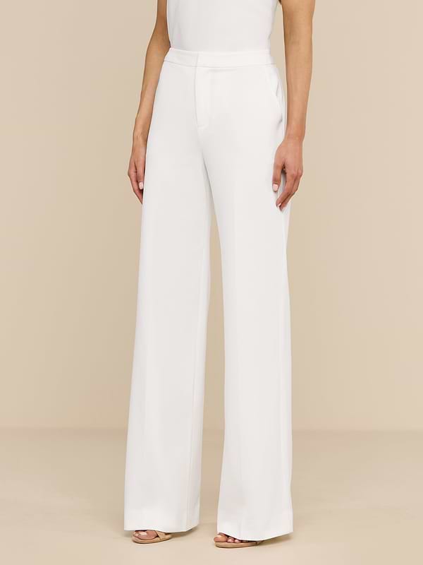 A woman stands against a plain white background, wearing the high rise, wide leg Livvy Trouser and a sleeveless white top. Only her body from the shoulders down is visible.