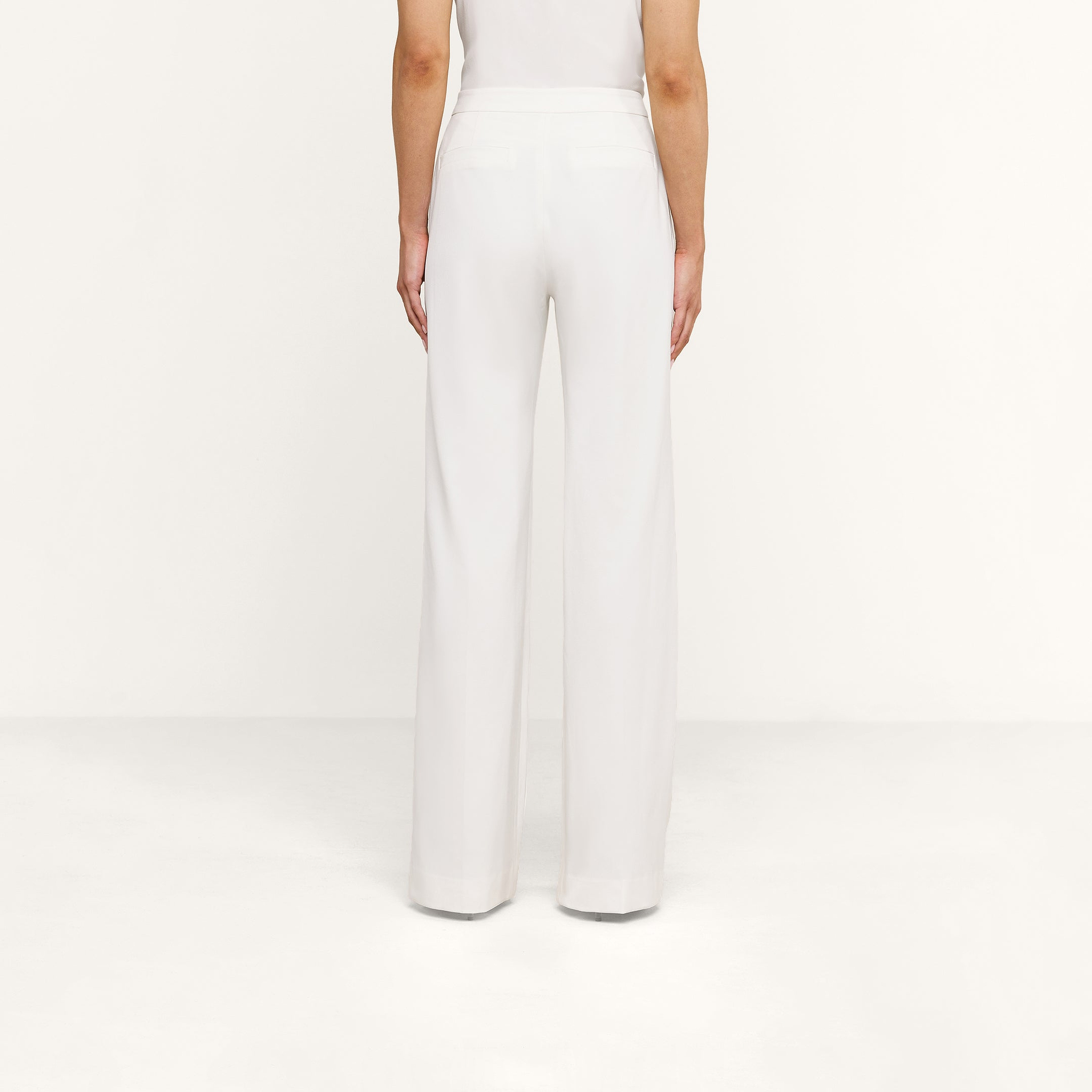 A person is shown from the back, standing against a white background, wearing high rise white Livvy Trouser and a white top.