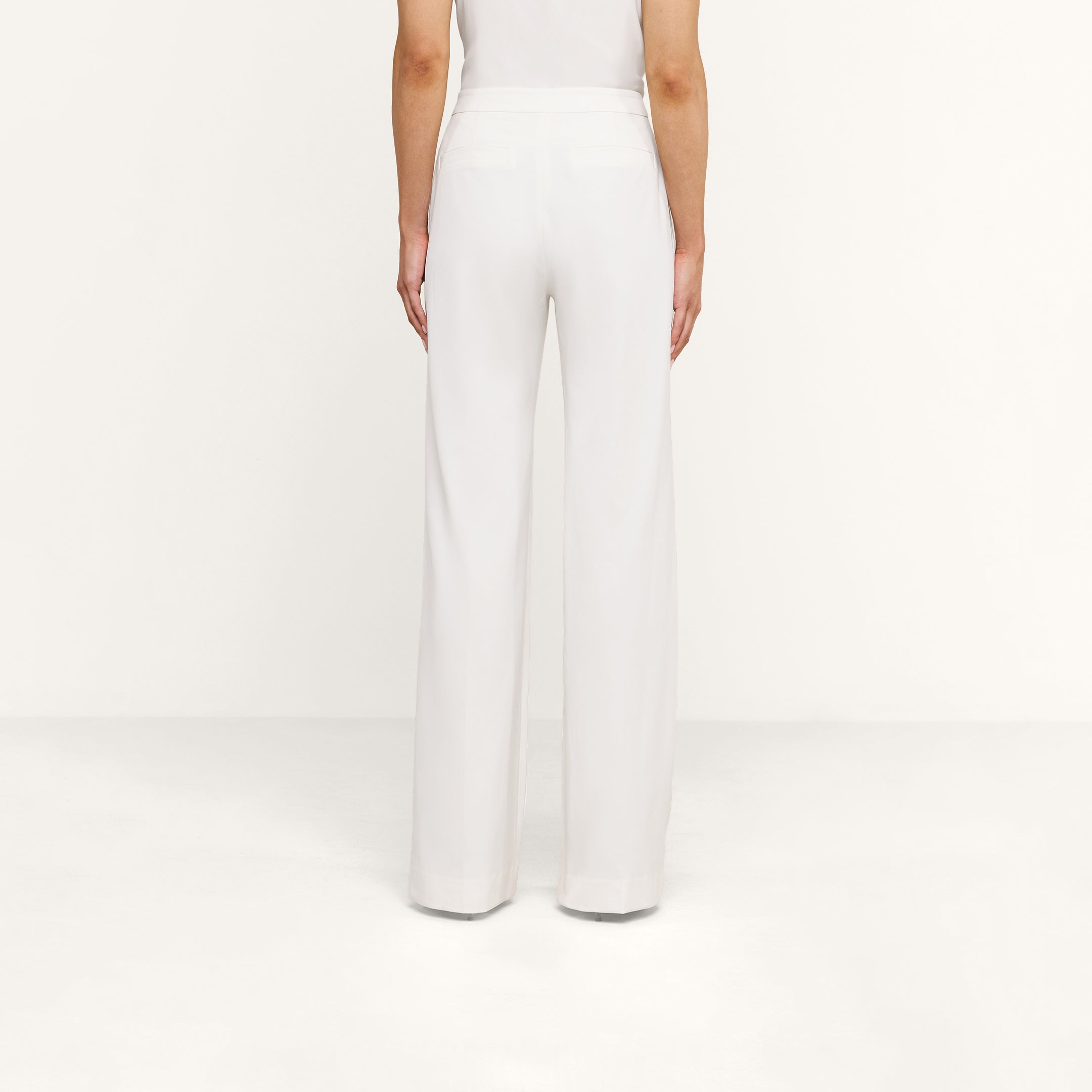 A person is shown from the back, standing against a white background, wearing high rise white Livvy Trouser and a white top.