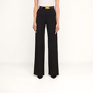 Indossando i pantaloni Livvy — un modello nero a vita alta e a gamba larga — abbinati a una cintura nera con una vistosa fibbia dorata, eleganti scarpe nere a punta e un top bianco senza maniche, questa persona posa su uno sfondo beige in un look chic e disinvolto, ideale per passare con disinvoltura dall’ufficio alla cena.