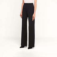 Wearing the Livvy Trouser in black—a high-waisted, wide-leg style—paired with a white top and black pointed-toe shoes, this look is set against a plain beige background, making it ideal for transitioning from the office to dinner.