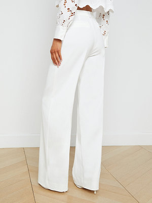 A woman stands on a light wood floor, shown from the back, wearing high-rise, wide-leg Livvy Trousers in white and a white long-sleeve lace top.