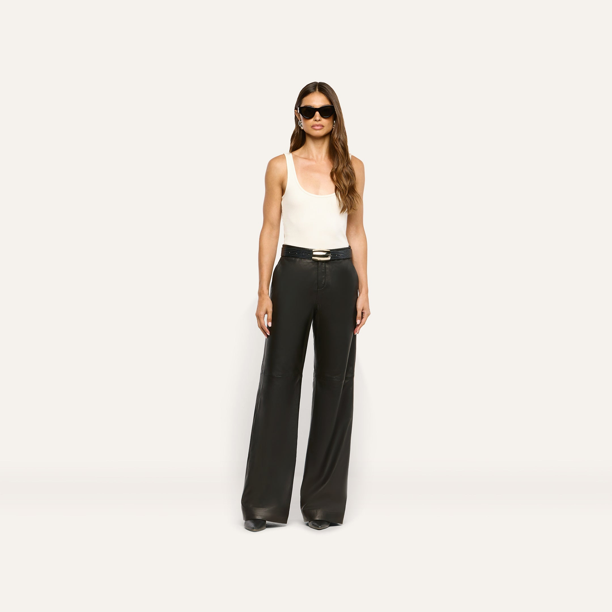 A person wearing a white tank top, black lambskin Livvy Leather Trouser wide-leg pants with a black belt, sunglasses, and pointed-toe heels.