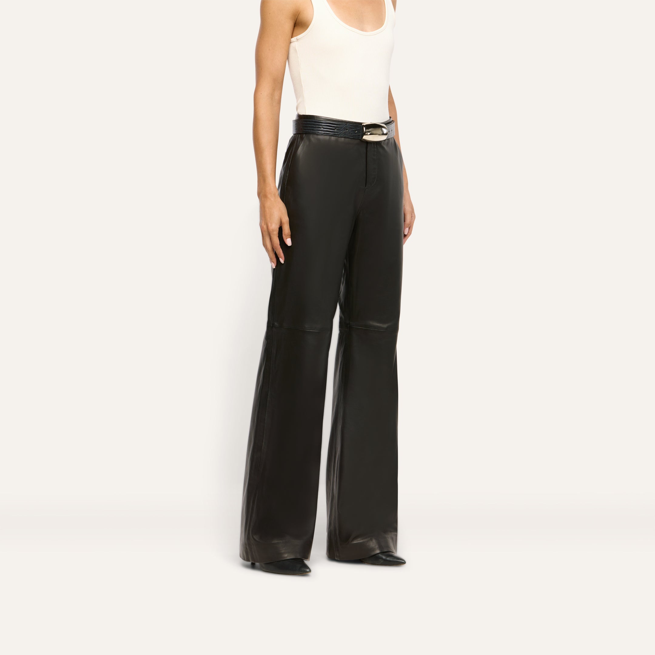 A person wearing black Livvy Leather Trouser straight-leg trousers, styled with a black belt and pointed-toe shoes.