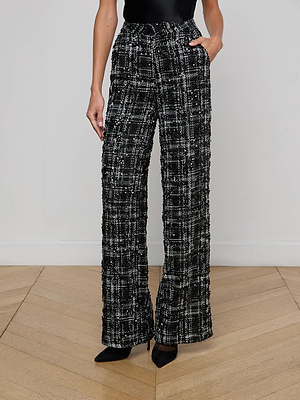 A person wearing the L'AGENCE Livvy Tweed Trouser in black and white plaid with a black top and pointed-toe heels stands on a light wood floor against a plain white wall.