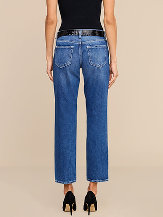 A person stands against a plain beige background, shown from the back, wearing the Nevia Slouchy Straight-Leg Jean in a blue medium-dark vintage-inspired wash, styled with a black belt, black sleeveless top, and black high heels.