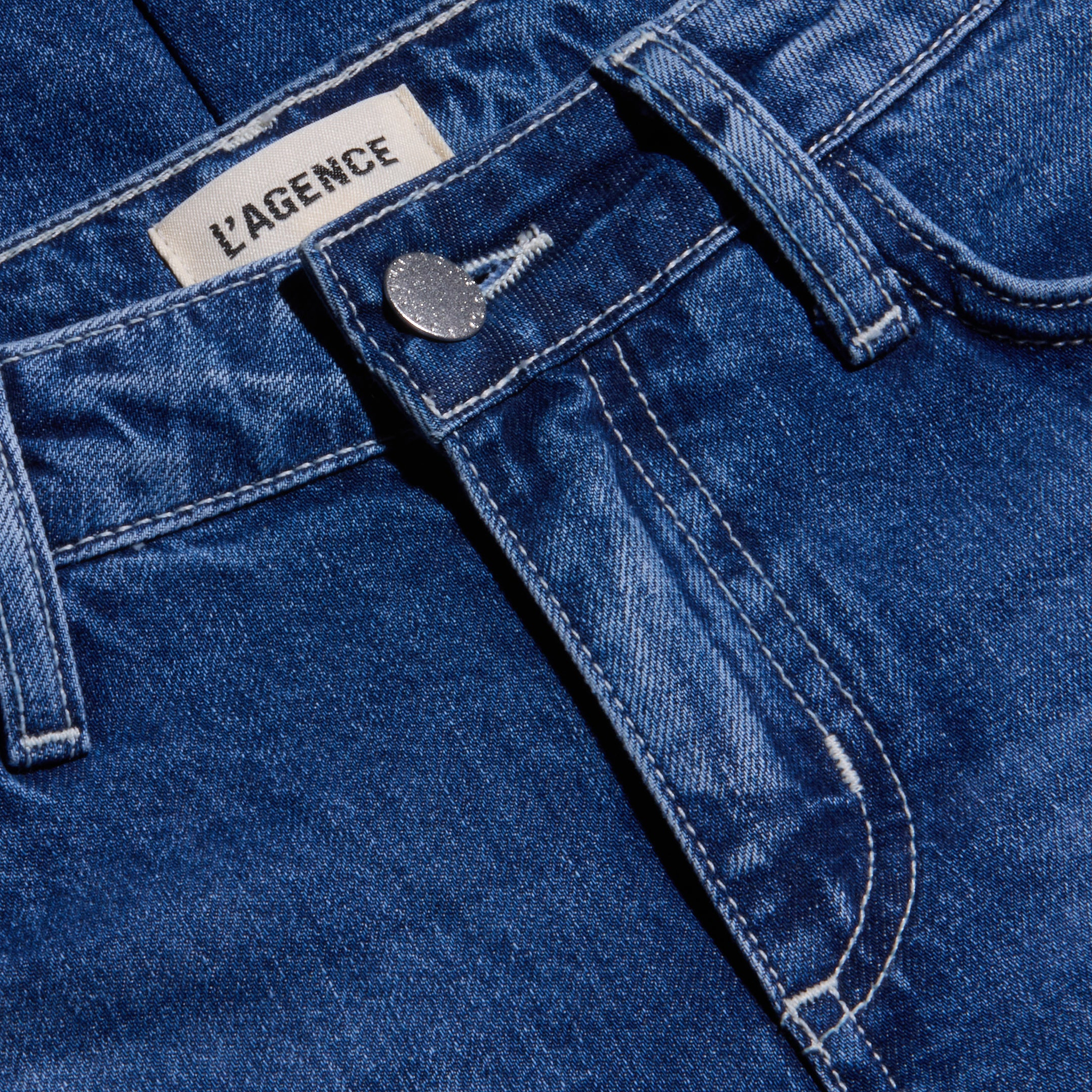 Close-up of the Nevia Slouchy Straight-Leg Jean in blue denim, showcasing a visible metal button, belt loops, and LAGENCE brand label on the waistband. Crafted from all-cotton denim with a classic textured pattern and contrast stitching, these jeans offer a vintage-inspired look.