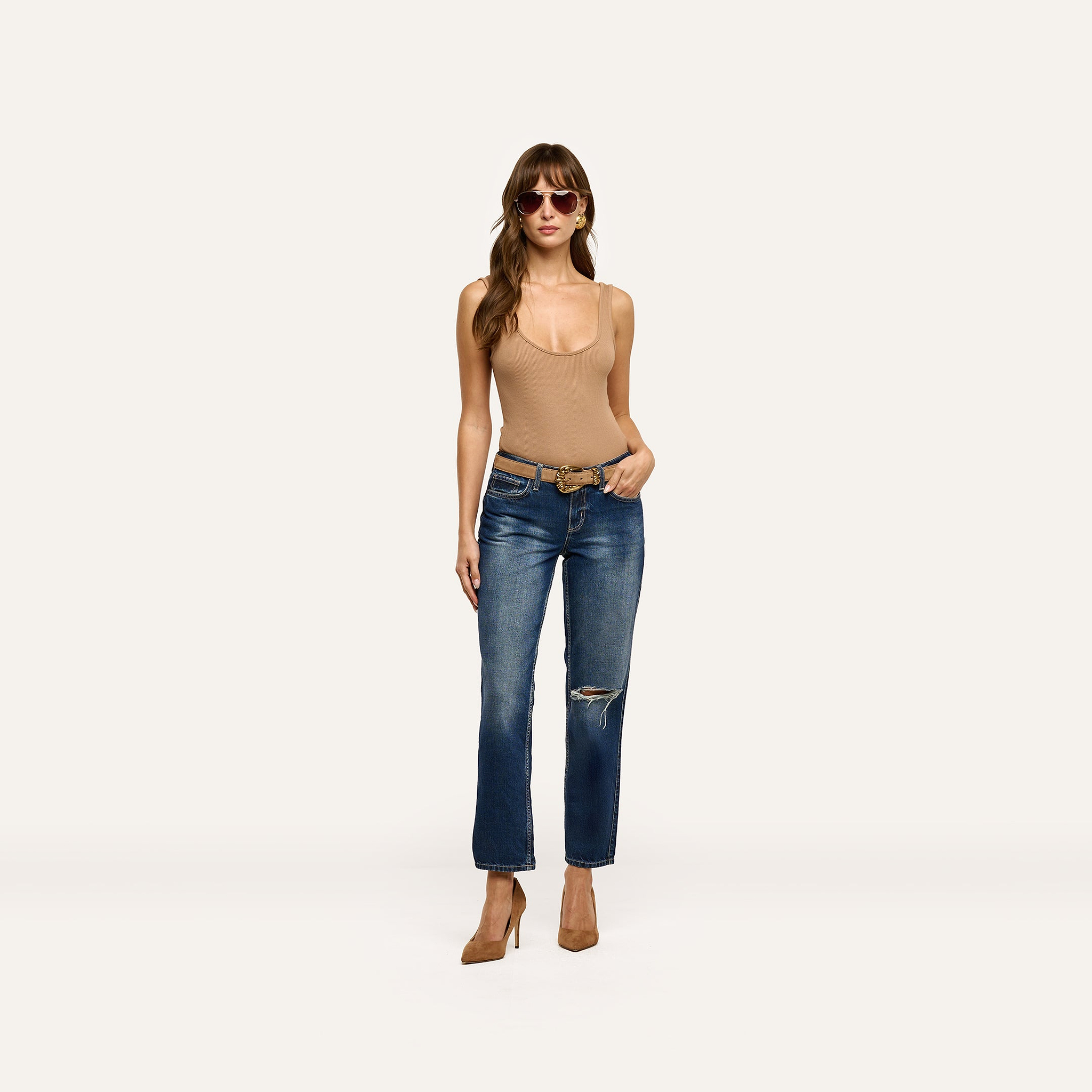 A woman wears a tan bodysuit, brown belt, and Nevia Slouchy Straight-Leg Jean with a distressed knee, styled with brown pointed-toe heels and oversized sunglasses.