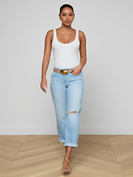 A woman confidently walks indoors on a wooden floor, styled in a white tank top, sandals, and the Nevia Slouchy Straight-Leg Jean against a plain white wall.
