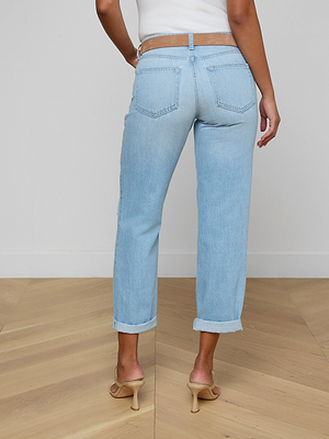 Wearing the Nevia Slouchy Straight-Leg Jean with a white top and beige heeled sandals, a person stands on a wooden floor, back to the camera. The vintage-inspired jeans feature back pockets and rolled-up ankles.