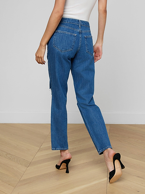 A woman in a white tank top and Nevia Slouchy Straight-Leg Jean stands on a wooden floor wearing black heels, with one leg slightly bent as she faces away from the camera.