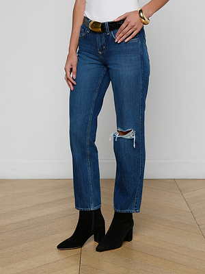 Wearing the Nevia Slouchy Straight-Leg Jean in dark blue with a knee rip, a black belt, gold bracelet, and black heeled boots, a person stands on a wooden floor by a white wall. Their face is not shown.