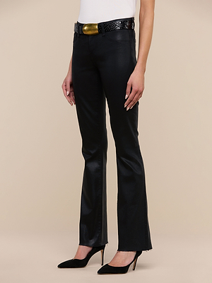 A person wears the Sneeki Coated Straight-Leg Jean in black, a white sleeveless top, a black textured belt with a large gold buckle, and black pointed-toe heels while standing against a beige background.