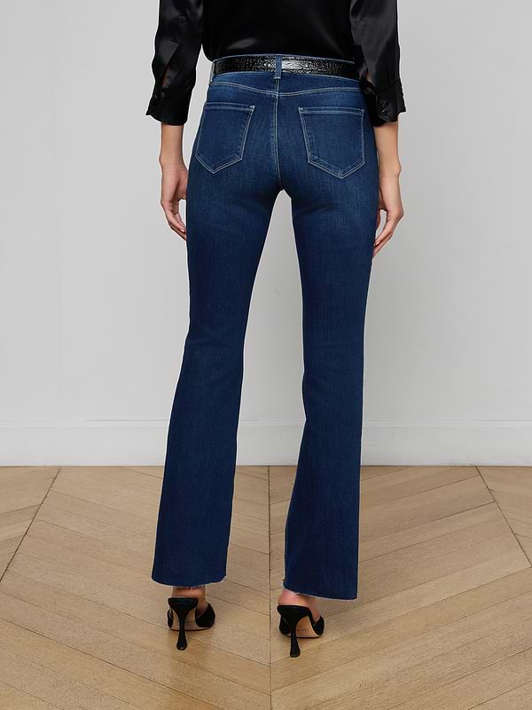 A person stands facing away, wearing a black sleeveless top, a pair of Sneeki Low-Rise Straight-Leg Jeans in dark wash super stretch denim with back pockets, a black belt, and black heeled shoes against a plain white background.