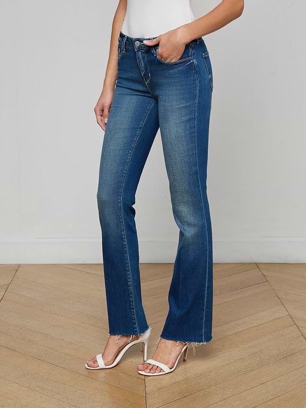A woman stands against a plain white background wearing Sneeki Low-Rise Straight-Leg Jeans in blue with frayed hems, styled with a brown belt, a dark sleeveless top, and beige heeled shoes.