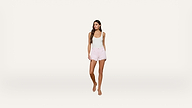 Woman wearing a white tank top, light pink shorts, and sandals stands against a plain white background, looking slightly to the side.