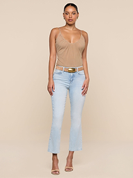 A woman faces forward against a beige background wearing the Tati Cropped Micro Boot Jean light wash, a tan sleeveless top, brown belt with gold buckle, and beige heeled sandals. Her hair is pulled back and she has a neutral expression.