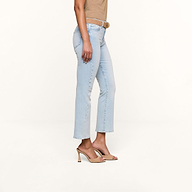 A person wearing Tati Cropped Micro Boot Jean, a brown belt, a beige top, and beige high-heeled sandals stands against a plain beige background.