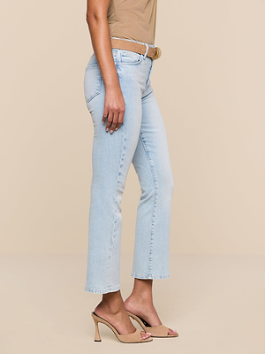 A person wearing Tati Cropped Micro Boot Jean, a brown belt, a beige top, and beige high-heeled sandals stands against a plain beige background.