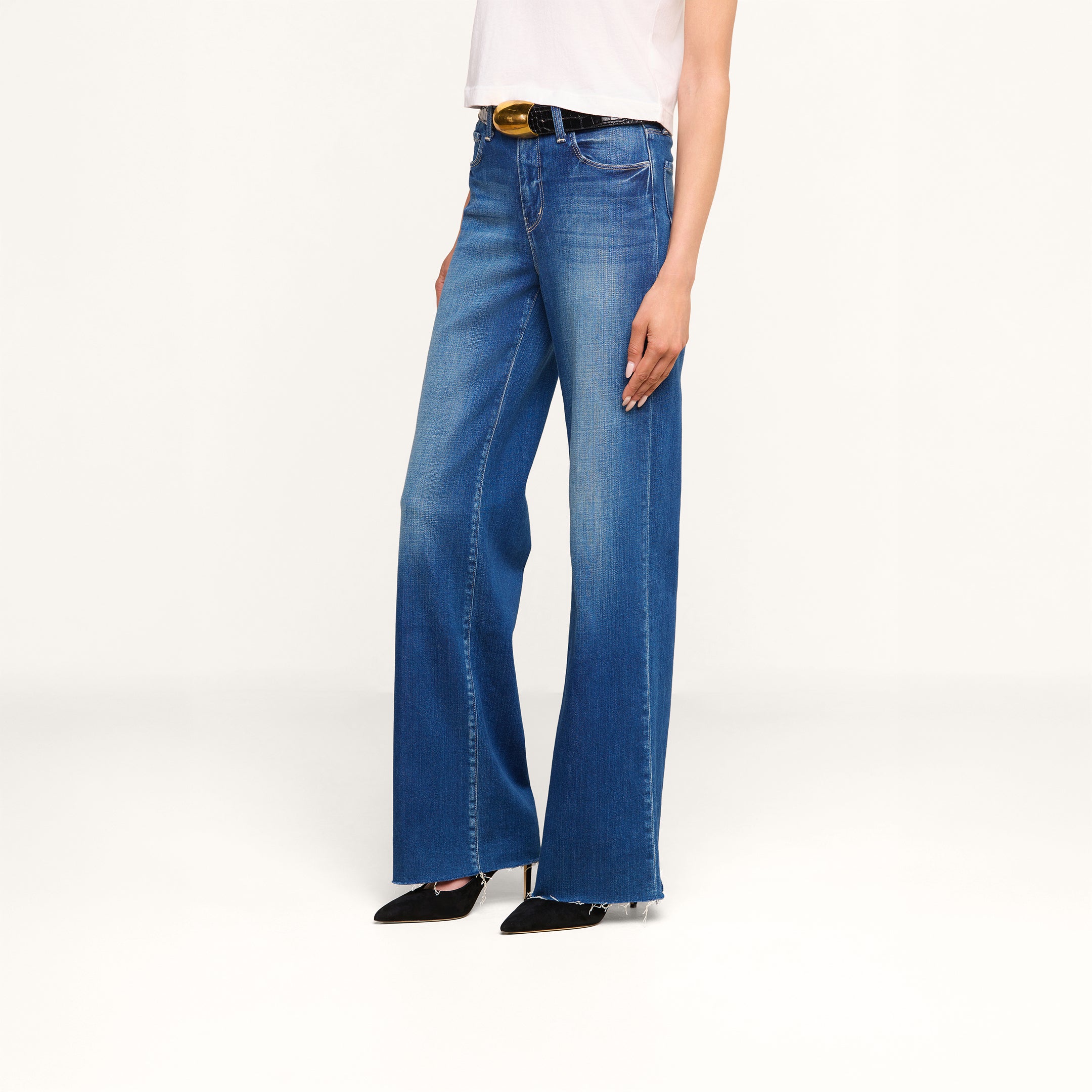 Person wearing Scottie Wide-Leg Jean, a white sleeveless top, black pointed-toe heels, and a black belt with a gold buckle, standing against a plain white background.